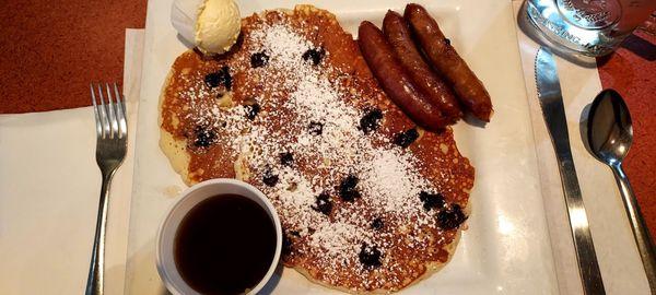 Two blueberry hot cakes with sausage, syrup, and butter