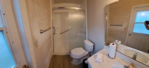 After Pictures: Walk-in shower with lower 3-inch barrier, frosted sliding glass doors, safety grab bars, new vinyl floor.