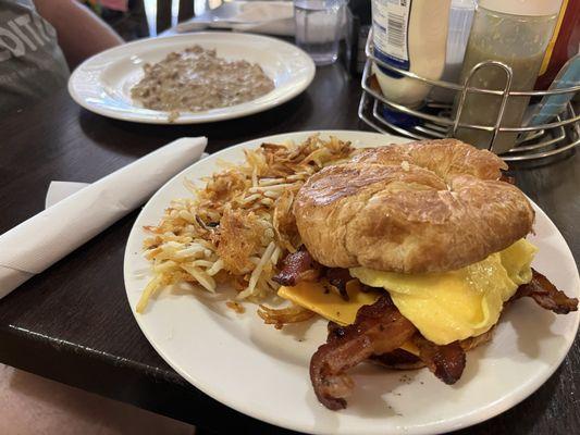 Bacon egg and cheese croissant , hash browns. A half order of biscuits n gravy in the background