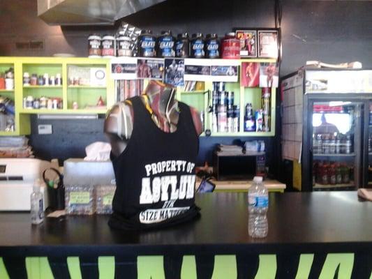 Front desk of The Asylum Gym. Displayed are the products available for purchase; an Asylum gym shirt and supplements.