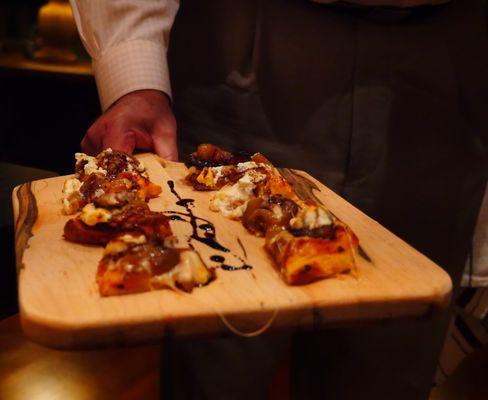 Bite-sized caramelized onion, goat cheese & sausage pizza ready for service with aged balsamic