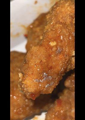 There's some sort of worm on this boneless chicken wing and some sort shiny stuff.