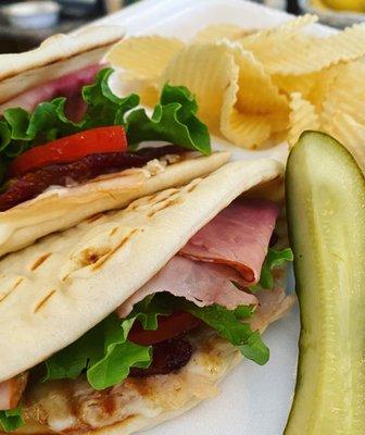 Ham sandwich on pita bread with chips and a pickle