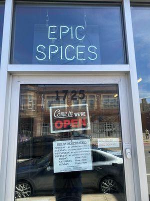 A tiny storefront with the hours posted on the front door.