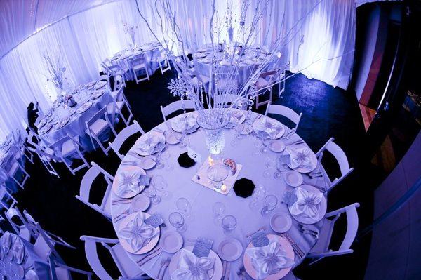 Formal table settings include white resin chairs, satin linens and napkins, chargers, flatware, elegant wine glasses and plates.