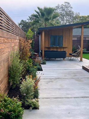 Studio with extended roof and pass through bar window, Ipe wood fence, concrete and mosaic tile patio, plantings