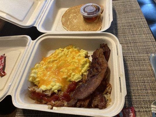 Traditional Breakfast with scrambled eggs and cheese on top, bacon, hashbrowns (I added the ketchup myself), and a pancake.