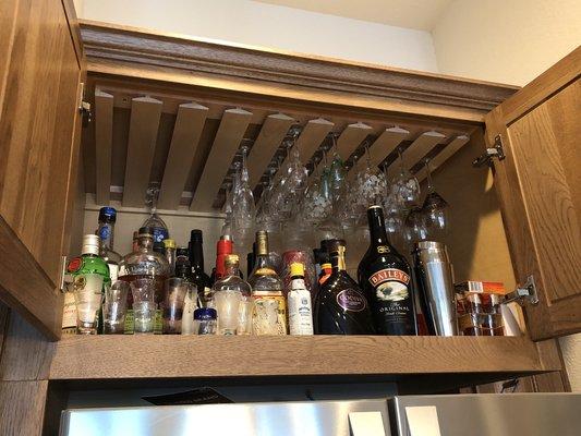 Custom stem glass holder and liquor cabinet above fridge.