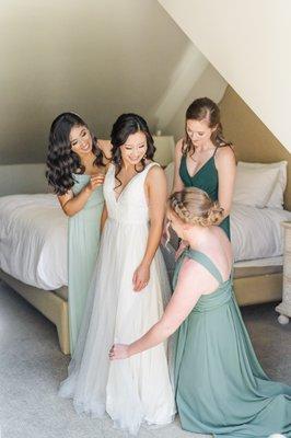 Bridesmaids help bride get dress and jewelry on