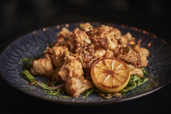 Cauliflower Tahina: Warm crispy cauliflower florets tossed in an tahini dressing over vinaigrette arugula, topped w/ pepitas & crush chilis.