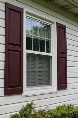 White double hung window on an off white siding with red shutters