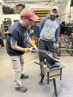 Drew instructs Aaron on how to craft the metal into a loop a loop