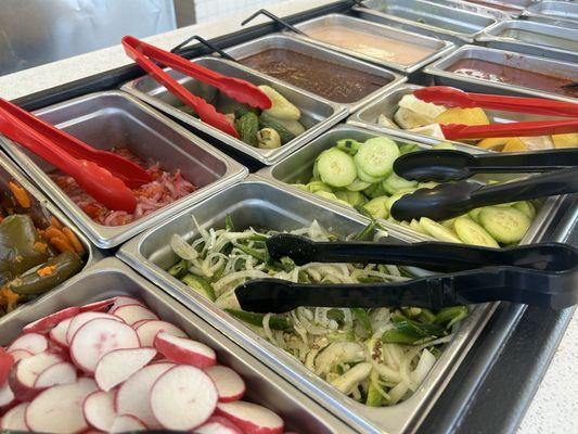 Condiment bar with various fresh and pickled veggies, and several salsas.