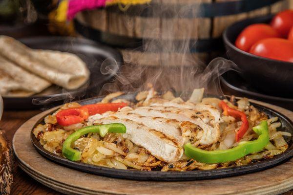 Chicken fajitas - served sizzling hot on a bed of sautéed onions and bell peppers, with refried beans,