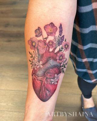 Realistic color anatomical heart and flowers on forearm.