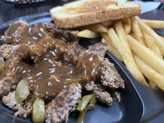 Chopped beef and gravy with green peppers and fries with a slice of bread