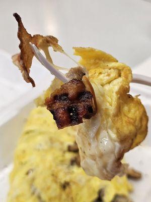 A close-up of a piece of my Omelette being held with a fork and a piece of bacon on the tip.