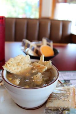 A cup of vegetable soup and crackers and more crackers and cheese.