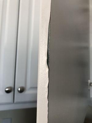 Delamination along the side of a cabinet door, well above the threshold for heat-related damage.