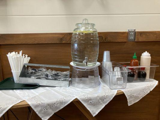 Self service: straws, plastic ware, water with lemon, cups, and sauces.