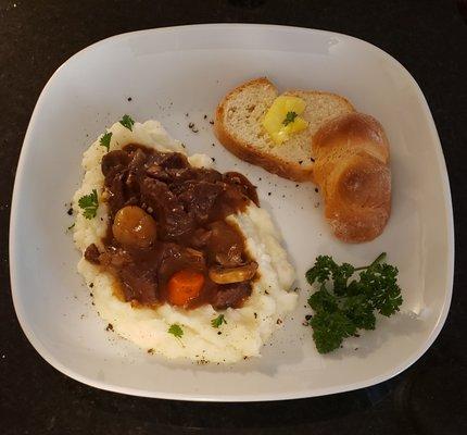 Beef Bourguignon - A delicious homemade beef bourguignon in a wine sauce served over mashed potatoes with a side of warm buttered bread.