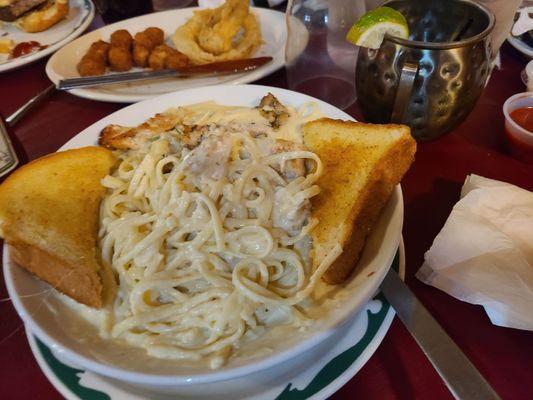 Fettuccine Alfredo with grilled chicken in the foreground with the onion rings and cheeseballs in the background