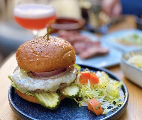 Wagyu Cheeseburger w/ cheddar, bibb, red onion, aoili, tomato, pickles | $18 (Background: Jimbo's Sour-$14)