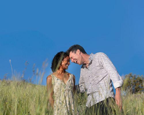 Adorable moment between interracial couple in a meadow. Both people are laughing.