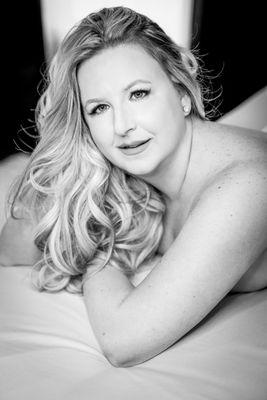 Black and white image of a woman posed looking at the camera for boudoir session set with sheets.