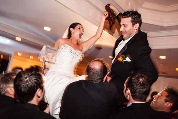 Wedding guests lift Jewish bride and groom on chairs to dance the Hora