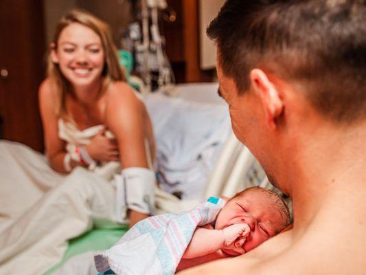 First time mom smiles as her husband holds their newborn baby immediately after birth at Boca Regional Hospital