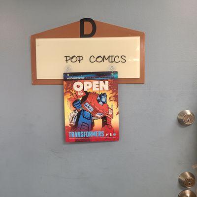 Blue Door that has D in black lettering about Pop Comics with a sign that says OPEN