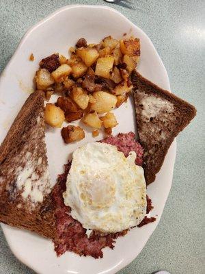 Egg over easy atop corned beef hash with home fries