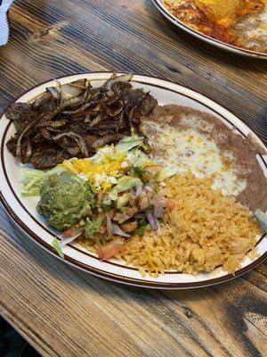 Carne asada plate with beans and rice a little salad with guacamole on top