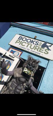 Werwolf standing in front of comic book store, books with pictures, holding a comic book in their mouth.