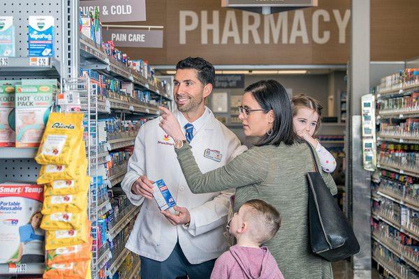 Customer with children asking advice from pharmacist in aisle.