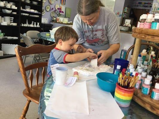 Owner helping young artist with saving cream technique on the pot he made in the clay room