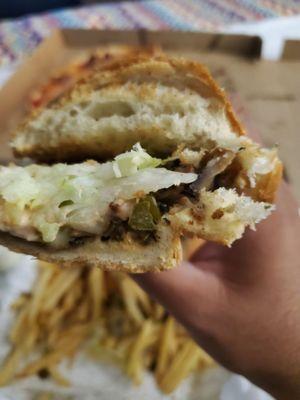 Side angle of the cheesesteak on a roll with lettuce, cheese, and peppers. Popping with flavor.