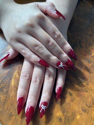 Dark red cranberry acrylic nails with white bows on the ring finger and a rhinestone in the middle of the bow