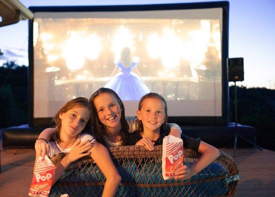 Girls enjoying our outdoor movie screen rental in the backyard with tasty popcorn!