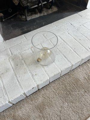 Part of a lamp that went into storage and they left the bulb and glass part on the ground by the fireplace.