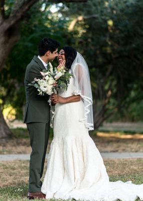 A bride and groom kiss while the bride holds flowes