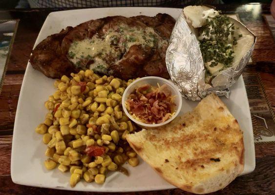 Ribeye steak, loaded baked potato, fire roasted corn, and garlic bread.