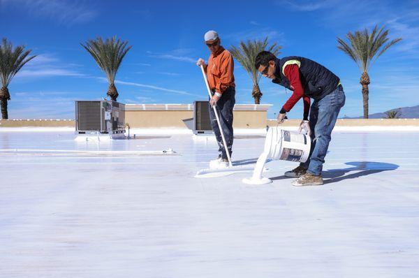 Roofer pouring fresh silicone on commercial roof.