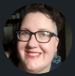 headshot of a female identified person with short hair, large dark glasses, red lipstick and a large smile.