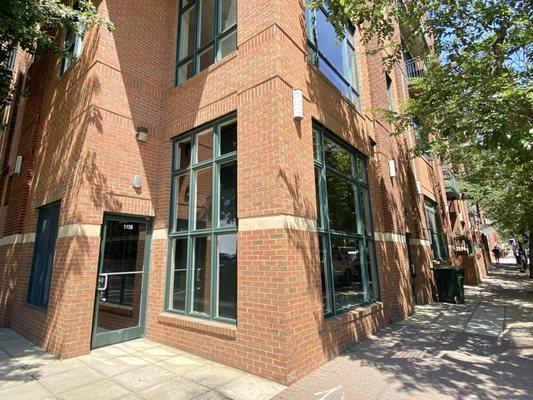 Multi-story red brick building. Large windows and doorway are framed in green.