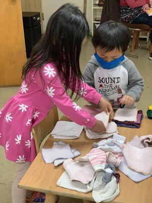 An older child and younger child work together to take care of the laundry in their classroom