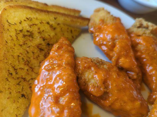 Chicken tenders with buffalo sauce and garlic bread on the side.