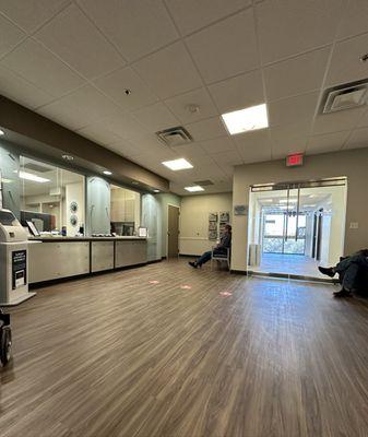 Big open area with kiosk check-in and front desks on the left. Chairs for patients all around.