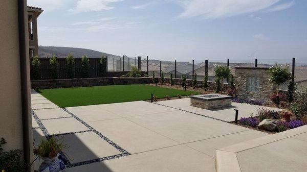 Etched concrete patio with stone insets. Artificial turf. Firepit with poured in place concrete top and Stone veneer water feature.